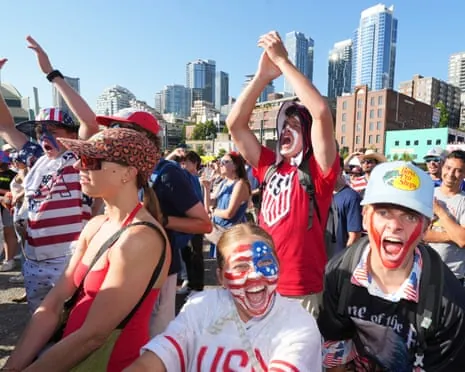 American fans, one with a painted flag on their face, smile during a celebration at the World Cup in Seattle.